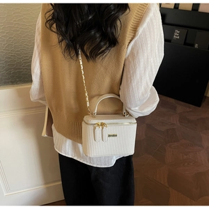 Detail of a beige woven mini bag with gold chain strap shown in a lifestyle setting
