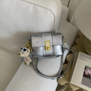 Détail du sac bandoulière tressé argenté avec boucle horloge vintage et breloque ourson