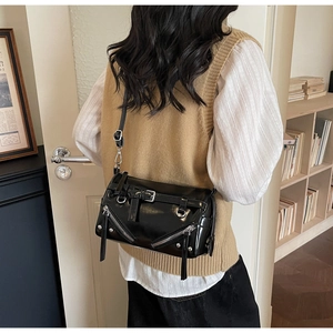 Close-up of a black glossy crossbody bag with metallic zippers and adjustable straps