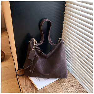 Macro detail of dark brown suede Hobo bag with gold zipper and a mini charm on wood