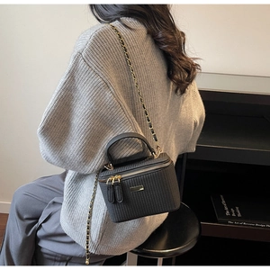 Detail view of the black textured crossbody bag with gold chain strap worn by a model