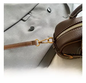 Detail of vintage gold metal hook on dark brown lychee leather bag with white stitching