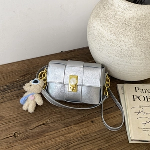 Détail d'un sac bandoulière argenté tissé avec boucle dorée et pendentif d'ours en peluche