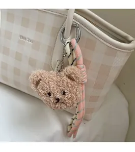 Close-up of a brown plush bear charm and woven rope on a checkered tote bag