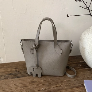 Détail d'un sac cabas en cuir gris grainé avec un pendentif éléphant sur un plan en bois