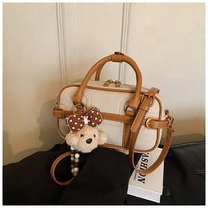 Detail of cream pebbled leather handbag with brown trim, golden hardware and plush bear charm