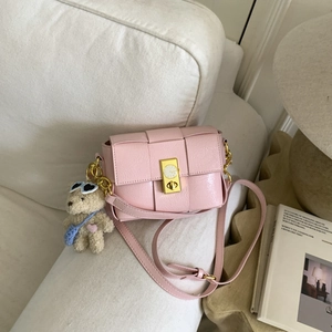 Détail d'un sac bandoulière rose tissé avec serrure dorée et breloque ours en peluche