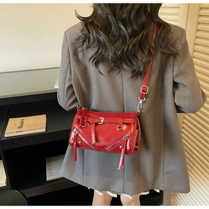Detail of red glossy leather crossbody bag featuring silver zippers and punk rivet studs
