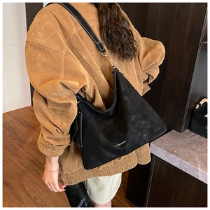 Detail of black suede tote bag with contrast strap and gold hardware on model