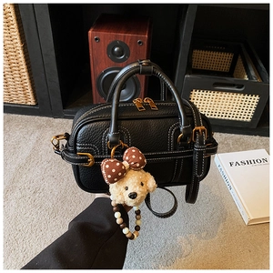 Close-up of black pebble leather handbag with white stitching and puppy plush charm
