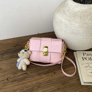 Détail du sac tressé rose avec serrure horloge dorée et breloque ours sur un banc