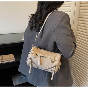 Detail of beige faux leather bag with silver zippers and rivets on a gray blazer model