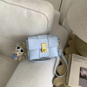 Vue détaillée d'un sac bandoulière tressé bleu clair avec fermoir doré et breloque ours