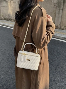 White woven crossbody bag with gold chain strap shown on model in outdoor street style setting