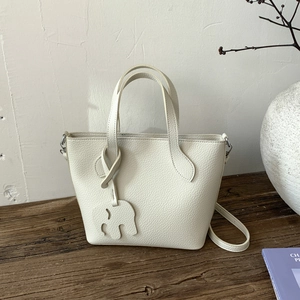 Détail du sac seau en cuir grainé blanc crème avec charm éléphant sur bois rustique