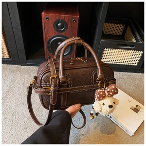 Detail of dark brown leather Boston bag with white stitching and plush dog charm