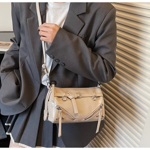 Detail of cream motorcycle-style crossbody bag with metallic zippers and silver hardware