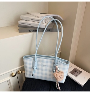 Détail d'un sac cabas à carreaux bleus avec logo blanc et pendentif ours en peluche marron