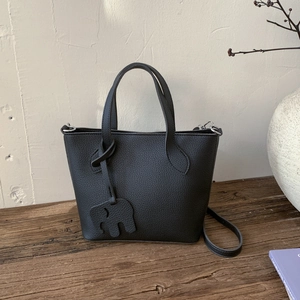Détail d'un sac cabas noir en cuir grainé avec charm éléphant dans un décor chaleureux