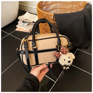 Close-up of beige lychee grain leather boston bag with black contrast trim and puppy charm
