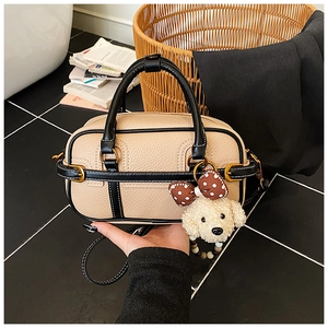 Detail of a beige Boston bag with black contrast trim and a cute plush dog pendant charm