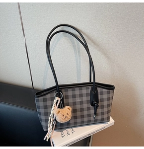 Detail of plaid tote bag with plush bear charm on white books in a cozy indoor setting