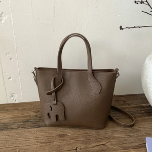 Détail d'un sac cabas en cuir marron foncé avec charm éléphant sur une surface en bois