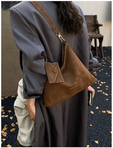 Detail of dark brown suede tote bag with a small matching envelope charm in outdoor setting