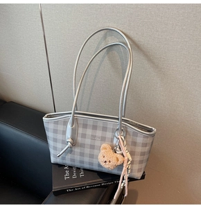 Detail of silver checkered tote bag featuring a plush bear charm on a leather sofa