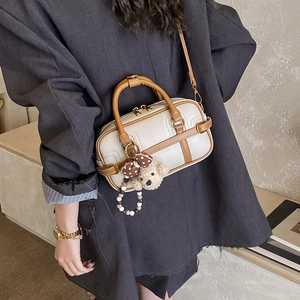 Mini beige boston bag with brown handles and plush bear charm shown on a grey blazer