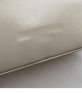 Macro dettaglio della trama in pelle crema e del logo del marchio goffrato in oro sulla borsa