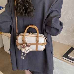 Close-up of white lychee leather bag featuring brown trim and a cute plush bear charm