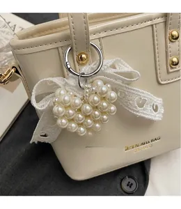 Dettaglio del ciondolo a cuore di perle con fiocco di pizzo su borsa a secchiello