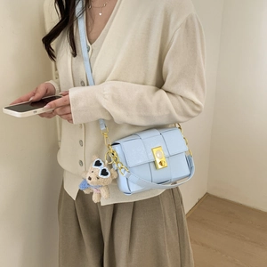 Détail du sac à bandoulière tressé bleu clair avec fermoir doré et breloque petit ours