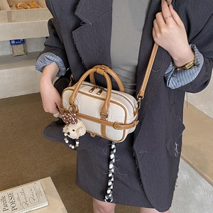 Detail of cream Boston bag with brown handles, metal zipper and plush puppy charm