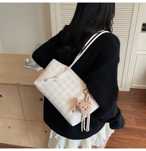 Detail of off-white checkered tote bag with a cute brown plush bear charm and thin straps