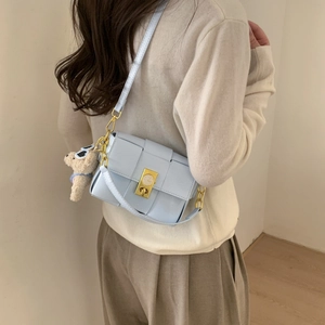 Détail du sac bandoulière tissé bleu clair avec boucle horloge et breloque ours