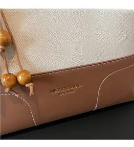 Detail of cream fabric and brown leather patchwork with gold embossed logo and wooden bead