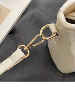 Dettaglio del gancio in metallo dorato lucido e cuciture precise sulla borsa crema