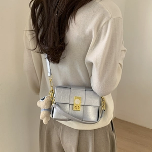 Détail du sac bandoulière en cuir tressé argenté avec fermoir doré et breloque ours