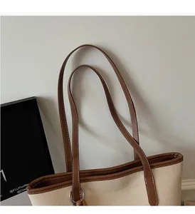 Close-up of beige canvas tote bag with brown faux leather handles and white stitching