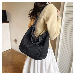 Large black denim tote bag with contrast stitching shown on shoulder in a cozy interior