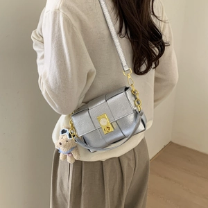 Détail du sac bandoulière tissé argenté avec boucle horloge dorée et breloque ours