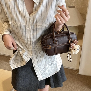 Detail of dark brown leather pillow bag with plush bear charm in a cozy indoor setting