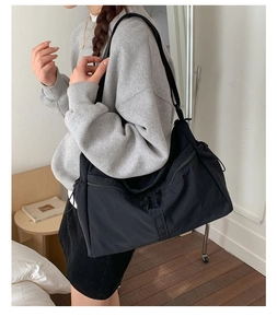Detail of a large black nylon dumpling bag featuring adjustable straps and zipper pockets
