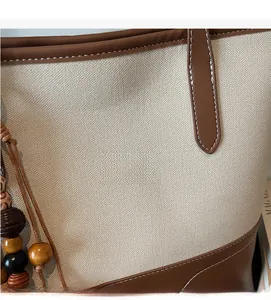 Close-up of off-white canvas tote bag with brown leather trim and neat contrast stitching