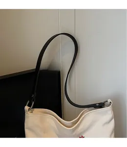 Detail of smooth black leather shoulder strap and silver metal hardware on canvas tote