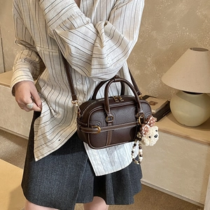Detail of dark brown pebble leather boston bag with stitching and plush bear charm