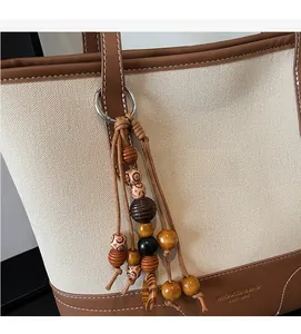 Detailed view of canvas tote bag featuring brown leather trim and a beaded wood charm