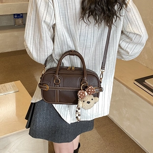 Close-up of brown textured leather crossbody bag with cute teddy bear charm on model